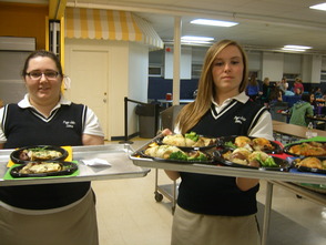 Christina Mendralla (left) and Hayley Kerrison (right), both members of Leadership Council and servers for Dinner Theater Night, are receiving their food to serve to parents.