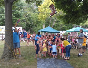Children stand in line to knock down a cowboy boot shaped piñata.