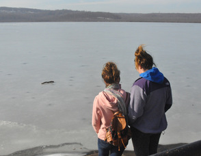 Two young girls stand by the lake.