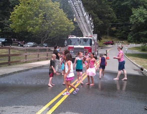 Children plays in the streets under a fire truck sprinkler.