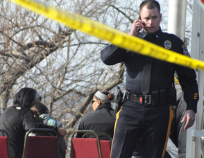 A police officer on the scene, as those allowed behind police lines wait beside the lake.