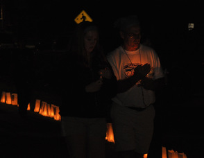 Two walkers proceed along the path with their candles.