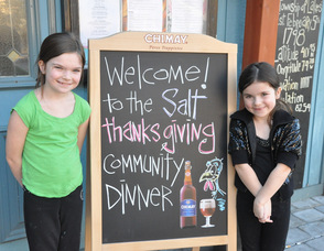 Milla and Tasha Hornung, ages 8, and 5, flank the community dinner welcome sign.